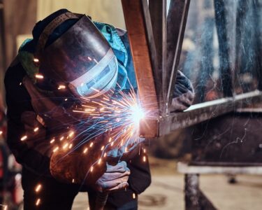 A skilled worker welding a rail segment in a metal fabrication workshop, with bright sparks flying from the welding point