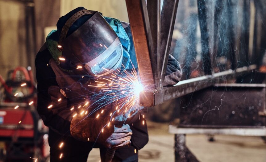 A skilled worker welding a rail segment in a metal fabrication workshop, with bright sparks flying from the welding point