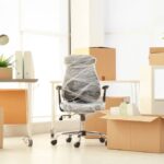 A newly furnished office space with moving boxes scattered around the space and the chairs wrapped in plastic.