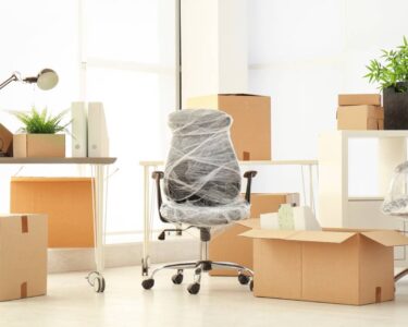 A newly furnished office space with moving boxes scattered around the space and the chairs wrapped in plastic.