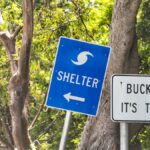 Two signs on a Florida road. One is blue and says "Shelter" with an arrow. The other is white and says "Buckle Up, It's the Law."