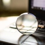 A black-handled magnifying glass rests on a black laptop's keyboard against a blurry meeting room background.