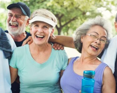 A group of diverse older adults wearing athletic clothes. They laugh with their arms wrapped around each other.