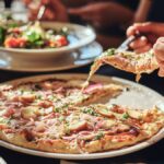 A group of people enjoying a meal at an Italian restaurant, eating pizza and a caprese salad with silverware.