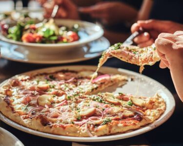 A group of people enjoying a meal at an Italian restaurant, eating pizza and a caprese salad with silverware.