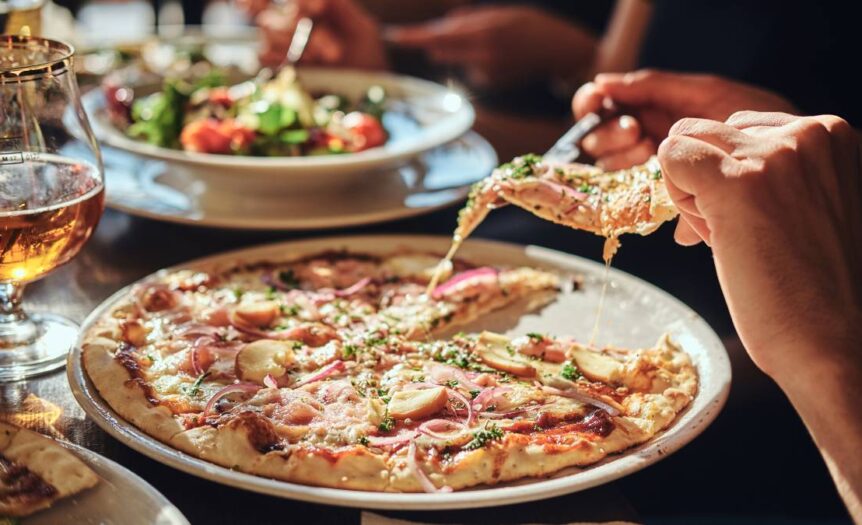 A group of people enjoying a meal at an Italian restaurant, eating pizza and a caprese salad with silverware.