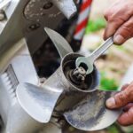 A boat's dirty outboard motor propeller. Two hands are holding a wrench and the propeller to loosen nuts and bolts.