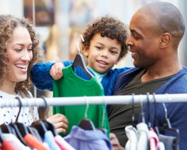 A mother, a father, and their young child browsing a selection of affordable kids’ clothing at a local store.