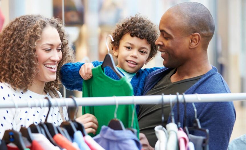 A mother, a father, and their young child browsing a selection of affordable kids’ clothing at a local store.