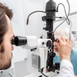 An eye doctor wearing a white lab coat checks a mature female patient's eyes during a routine eye exam.