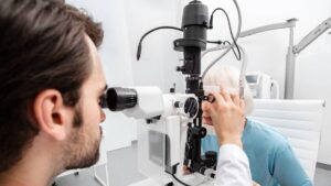 An eye doctor wearing a white lab coat checks a mature female patient's eyes during a routine eye exam.