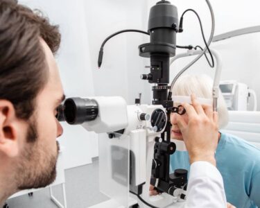 An eye doctor wearing a white lab coat checks a mature female patient's eyes during a routine eye exam.