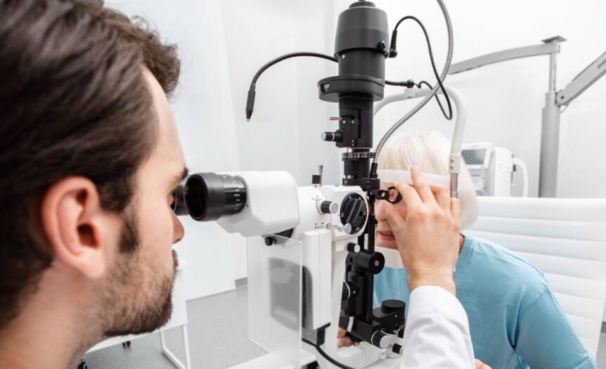 An eye doctor wearing a white lab coat checks a mature female patient's eyes during a routine eye exam.