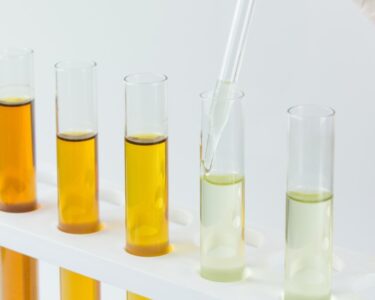 A row of tubes with different types of oil in them. A person with a glove is holding a dropper in one of the tubes.