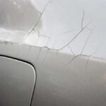 The back-left side of a gray car shows signs of cracking paint. Multiple lines spread from a spot above the fuel door.