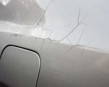 The back-left side of a gray car shows signs of cracking paint. Multiple lines spread from a spot above the fuel door.