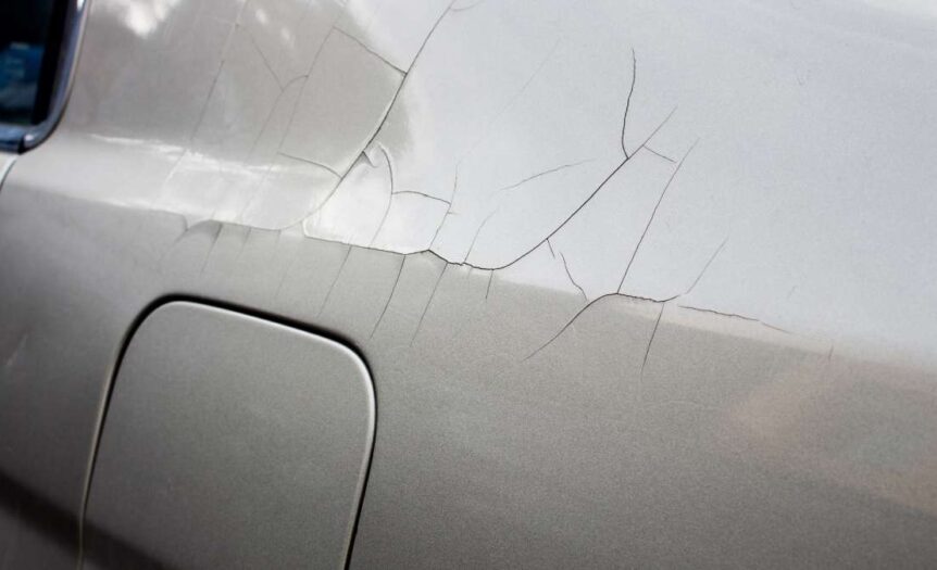 The back-left side of a gray car shows signs of cracking paint. Multiple lines spread from a spot above the fuel door.