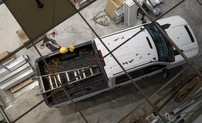 A person is talking on their phone while standing next to a pickup truck that is holding a ladder in the truck bed.