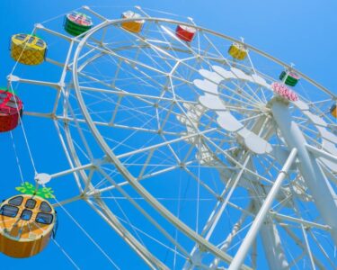 A Ferris wheel against a clear blue sky. The carriages are stylized in different fruits to look like oranges and watermelons.