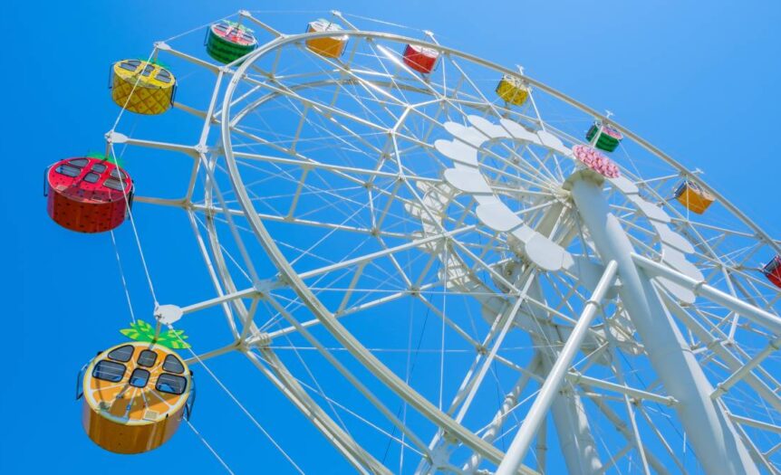 A Ferris wheel against a clear blue sky. The carriages are stylized in different fruits to look like oranges and watermelons.