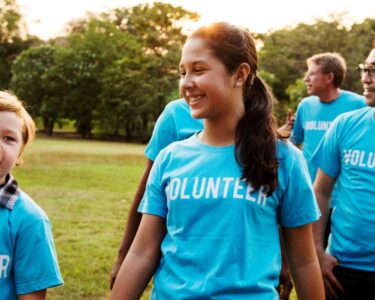 A group of people standing outside while wearing blue t-shirts with white lettering that says "Volunteer" across the chest.