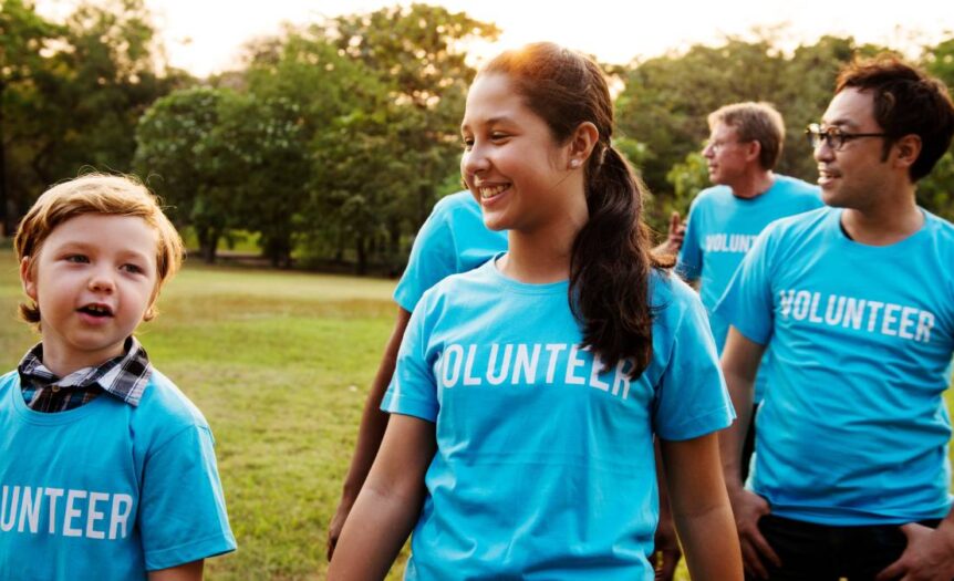 A group of people standing outside while wearing blue t-shirts with white lettering that says "Volunteer" across the chest.