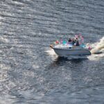 Aerial shot of a small boat out on the water with a wake behind it. Tied to the boat are several colorful balloons.