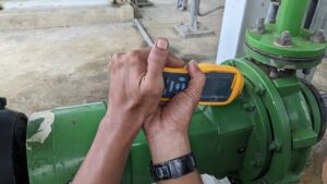 A man’s hands operating a portable vibration analysis device to maintain safety and efficiency in the industrial environment.