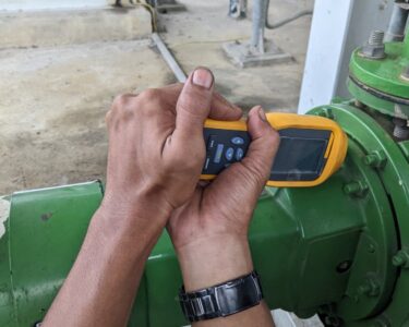 A man’s hands operating a portable vibration analysis device to maintain safety and efficiency in the industrial environment.