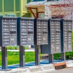 A row of cluster mailboxes stationed in front of a row of townhouses near a patch of grassy lawn and a tree.