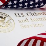 Two American flags are placed on top of a piece of paper that says "U.S. Citizenship and Immigration Services" in gold foil.