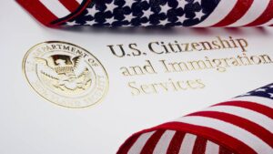 Two American flags are placed on top of a piece of paper that says "U.S. Citizenship and Immigration Services" in gold foil.