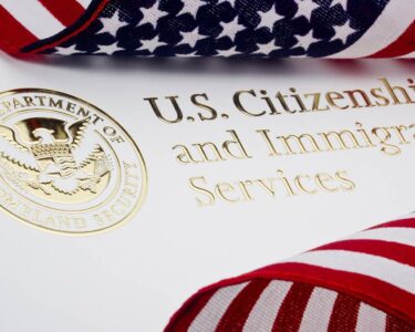 Two American flags are placed on top of a piece of paper that says "U.S. Citizenship and Immigration Services" in gold foil.