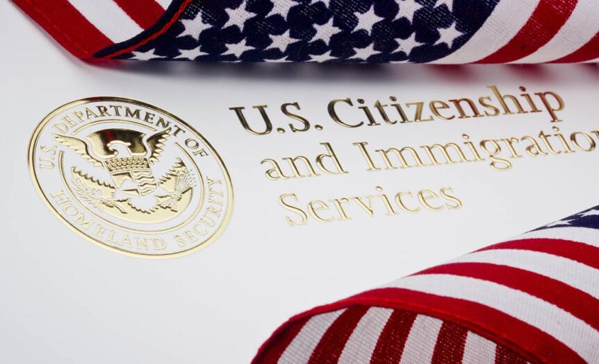 Two American flags are placed on top of a piece of paper that says "U.S. Citizenship and Immigration Services" in gold foil.