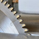 A close-up of a metal circular blade with large toothed edges. The blade is cutting a piece of metal.