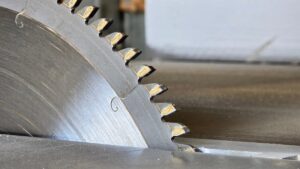 A close-up of a metal circular blade with large toothed edges. The blade is cutting a piece of metal.