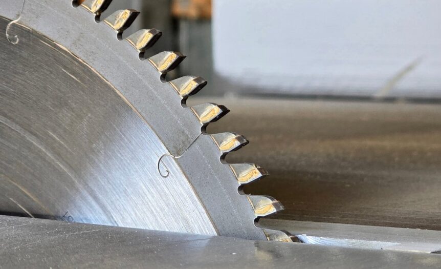 A close-up of a metal circular blade with large toothed edges. The blade is cutting a piece of metal.