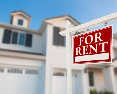 A red sign outside of a home labeled “For Rent.” It is a two-story house with a large garage and entryway.