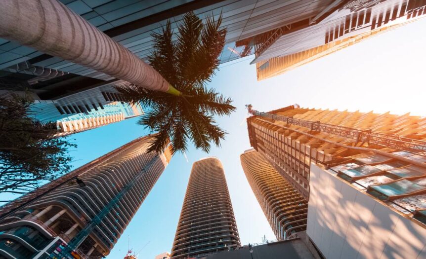 A skyward view of towering skyscrapers and palm trees in downtown Miami on a bright, sunny day.