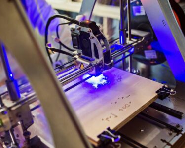 A laser engraving machine emits a bright blue light as it engraves a material. The background is blurry.