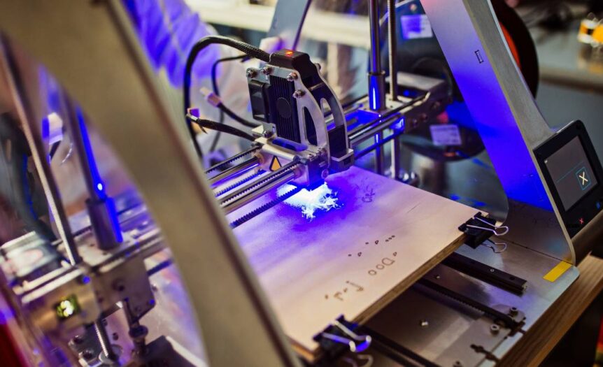 A laser engraving machine emits a bright blue light as it engraves a material. The background is blurry.