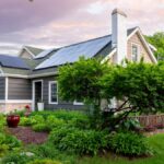 A lovely home surrounded by many leafy green trees and bushes is outfitted with rooftop solar panels.