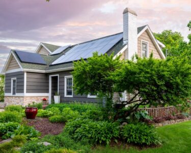 A lovely home surrounded by many leafy green trees and bushes is outfitted with rooftop solar panels.