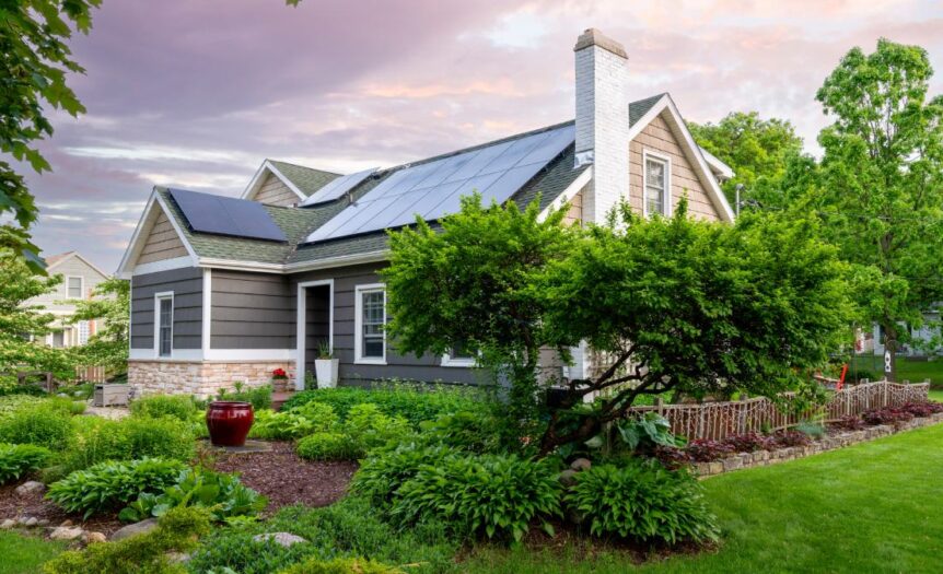 A lovely home surrounded by many leafy green trees and bushes is outfitted with rooftop solar panels.