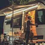 A man looking into the open side of his campervan. There is an awning attached to the van and a small table set up outside.