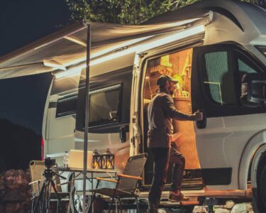 A man looking into the open side of his campervan. There is an awning attached to the van and a small table set up outside.