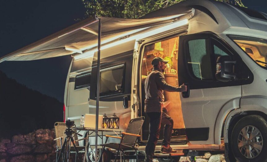 A man looking into the open side of his campervan. There is an awning attached to the van and a small table set up outside.