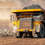 A big yellow mining truck hauls material out of a quarry while another truck appears to drive down the road.