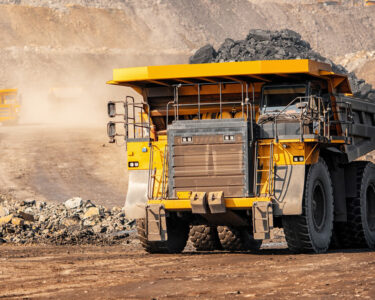 A big yellow mining truck hauls material out of a quarry while another truck appears to drive down the road.