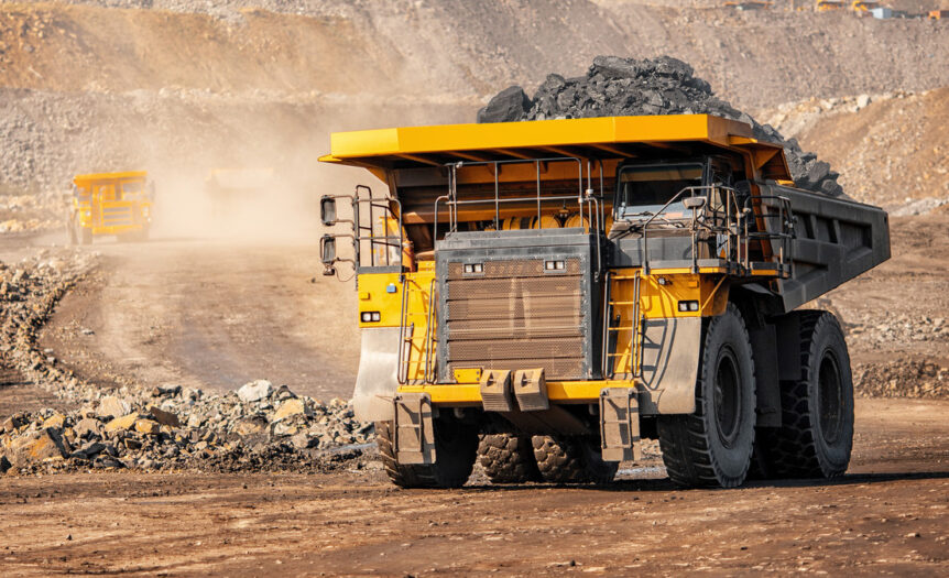 A big yellow mining truck hauls material out of a quarry while another truck appears to drive down the road.